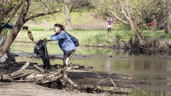 Jugendliche sammeln Müll an einem Fluß ein.