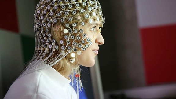 Das Profil einer blonden jungen Frau mit einer EEG-Kappe auf dem Kopf. Die Kappe besteht aus 250 runden Elektroden.