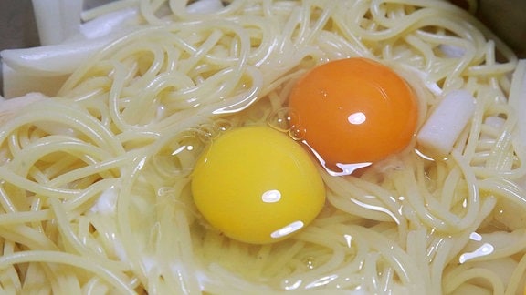 zwei aufgeschlagene Eier auf Spaghetti. Ein Eidotter ist leicht gelb, der andere dunkel-orange