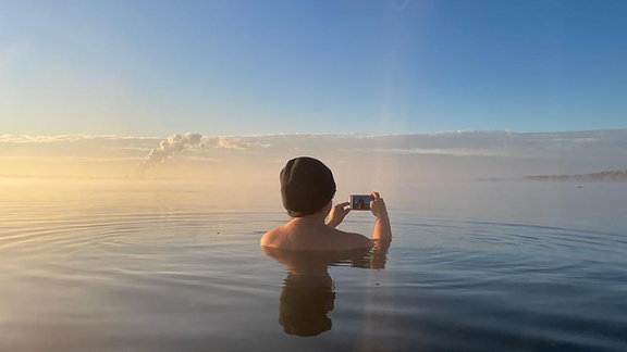 Eine Frau mit Mütze macht beim Eisbaden ein Foto