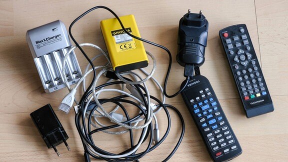 Akkuladegerät, Akkulader, USB-Kabel, TV Fernseher, Fernbedienung, Netzstecker liegen auf einem Tisch.