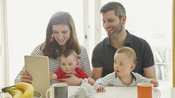 Eltern mit Kindern am Tisch und schauen auf ein Tablet