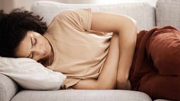 Frau liegt mit Bauchschmerzen auf einem Sofa