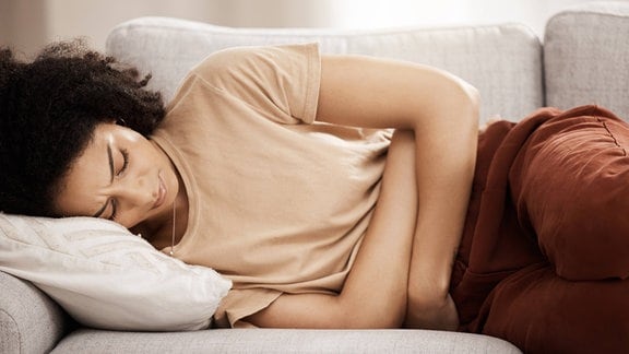 Eine Frau liegt mit Bauchschmerzen auf einem Sofa.
