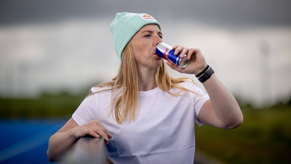Eine Frau mitr Mütze trinkt aus einer Dose Red Bull.