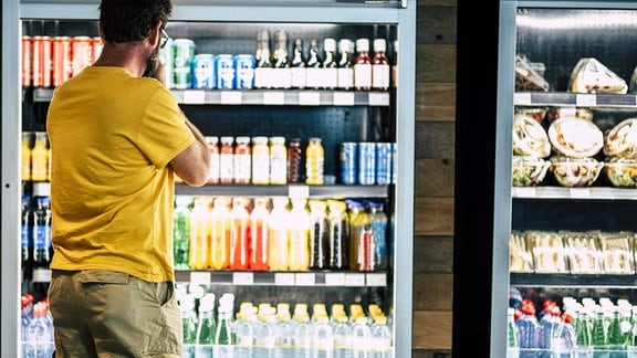 Ein Mann schaut im Supermarkt auf einen Kühlschrank mit Getränken.
