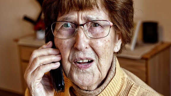 Seniorin zuhause beim Telefonieren schaut verängstigt.
