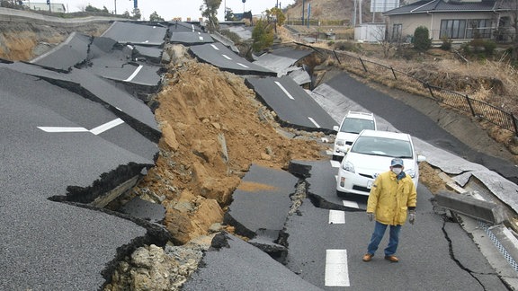 Eine Person steht auf einer von einem Erdbeben zerstörten Straße.