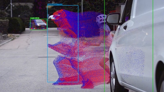 Das Bild zeigt sowohl Farbinformationen von der Farbkamera als auch Detektionen (blaue und rote Punkte) von der Ereigniskamera, die von einer rennenden Fussgängerin erzeugt werden
