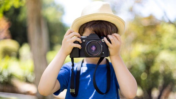 Kleiner Junge, der im Park ein Foto mit der Kamera macht.