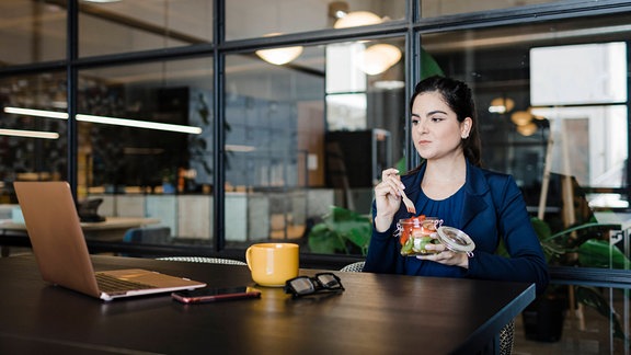 Eine Junge Geschäftsfrau die isst im Büro.