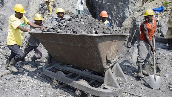 Wolfram Abbau in Ruanda. Männer schieben eine beladene Lore mit der Hand durch eine Mine. 