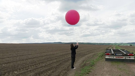 Eine Person steht neben einem Feld und hält einen Ballon an einer Schnur.