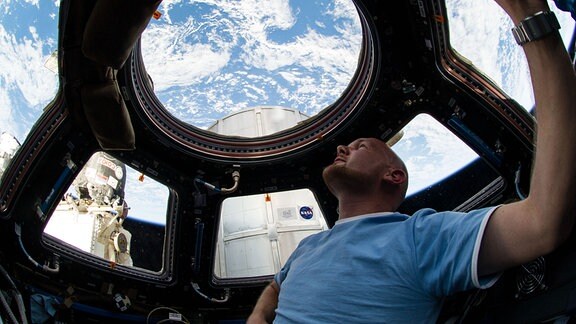 Alexander Gerst schaut aus der Raumstation auf den blau leuchtenen Erdball.