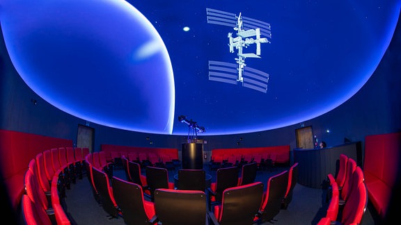 Ansicht des Sternensaals im Planetarium Halle. Auf die Full-dome-Kuppel ist die Animation eines Satelliten projiziert.