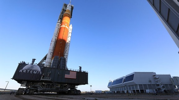 Das Vehicle Assembly Building der NASA am Space Center. Dessen Tore sind geöffnet und bereit für das herausrollen der SLS-Mondrakete. Zu diesem Zeitpunkt kann man aber nur den Turm, an dem die Rakete befestigt ist, erkennen.