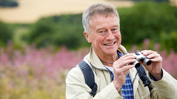 Ein Mann mit Fernglas steht in der Natur.