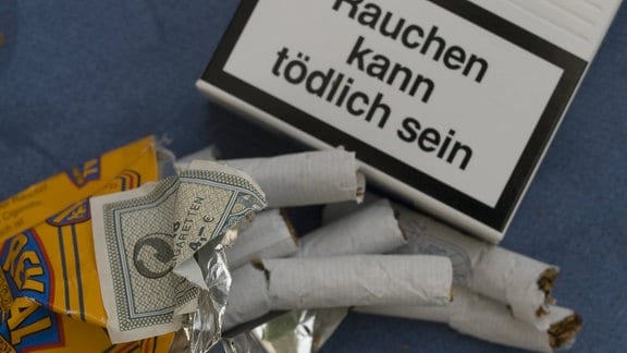 Zerknüllte Packung filterlose Reval-Zigaretten neben dem Warnhinweis einer anderen Zigarettenschachtel 