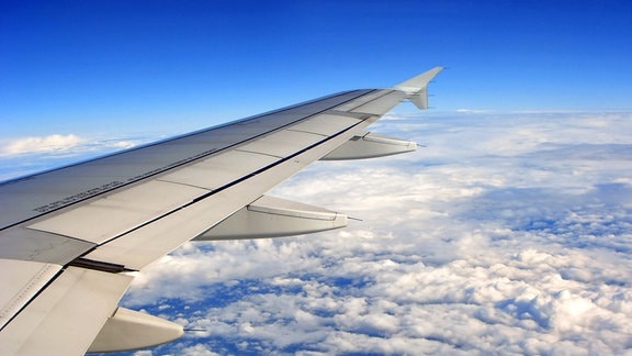 Flugzeuflügel vor blauem Himmel über der Erde und den Wolken, aus Flugzeugfenster gesehen.