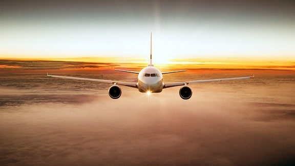 Fliegendes Flugzeug von vorn über den Wolken mit Sonnenuntergangsstimmung und rot-organge gefärbten Wolken im Hintergrund und darunter.
