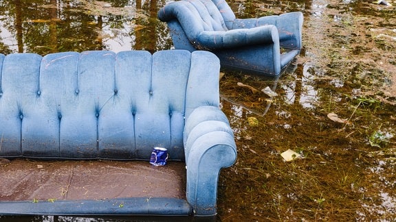 Sofa und Sessel schwimmen draußen in überflutetem Gebiet, Getränkedose auf Sofa.