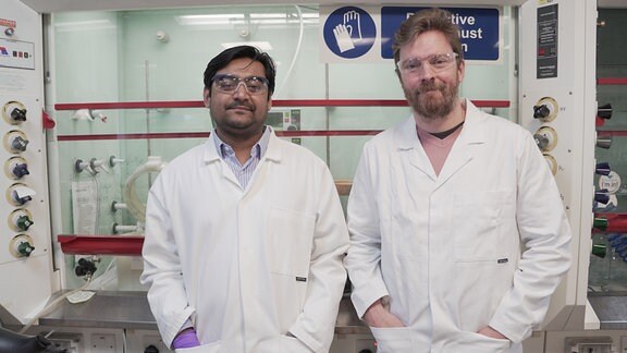 Zwei männliche Wissenschaftler in Kitteln in einem Labor. 