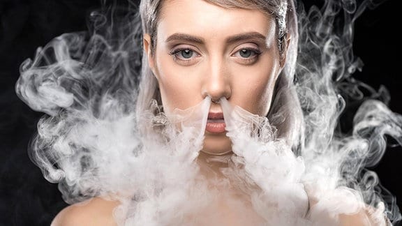Eine junge Frau läßt den Dampf einer E-Zigarette durch die Nase raus