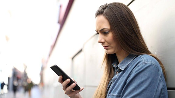 Eine junge Frau schaut mit gerunzelter Stirn auf ihr Smartphone.
