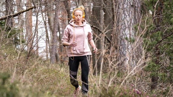 Junge Frau joggt durch hügeligen Wald und hört dabei Musik mit Kopfhörern, Ansicht von vorn