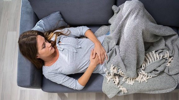 Frau liegt mit Bauchschmerzen auf einem Sofa.