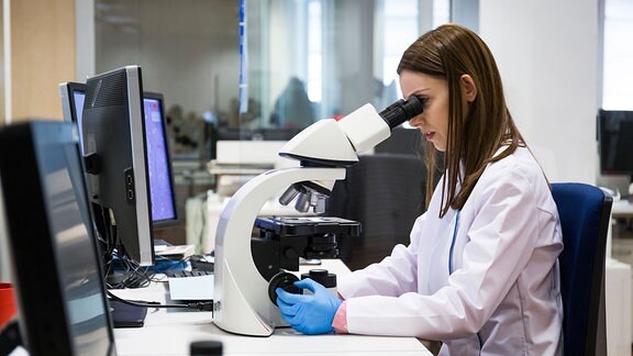 Eine junge Frau sieht durch ein Mikroskop