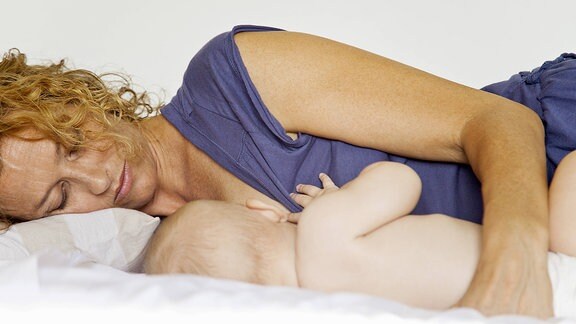 Eine Frau liegt auf einem Bett und stillt ihr Baby