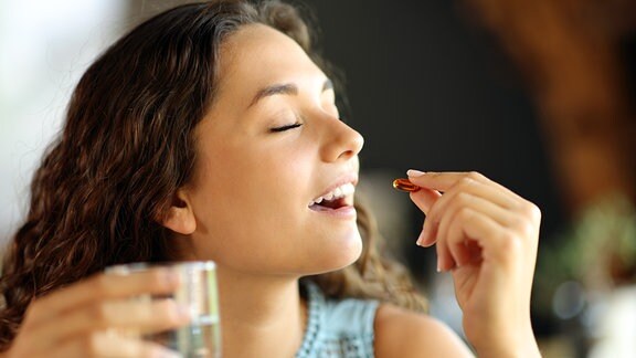 Eine junge Frau nimmt freudig eine Vitaminpille zu sich.