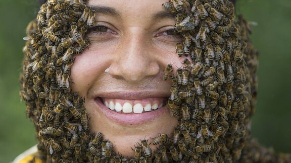 Viele Bienen sitzen auf dem Gesicht einer Frau und formen einen Bart.