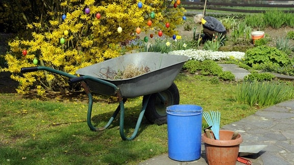 Eine Frau arbeitet in einem Garten, davor Utensilien für die Gartenarbeit