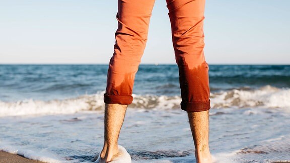 Mit den Füßen im Wasser steht ein Mann am Strand.