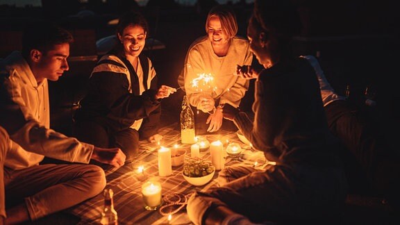 Freunde sitzen nachts auf einer Decke im Garten.Kerzen brennen.