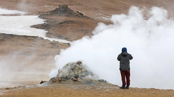 Ein Tourist fotografiert dampfende Fumarole.