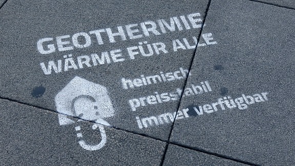 Auf einem Gehweg steht der Schriftzug: "Geothermie - Wärme für alle - heimisch, preisstabil, immer verfügbar"
