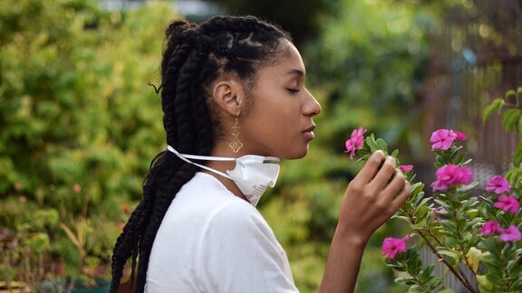 Junge Frau hat die FFP2-Maske abgenommen um an Blumen zu riechen