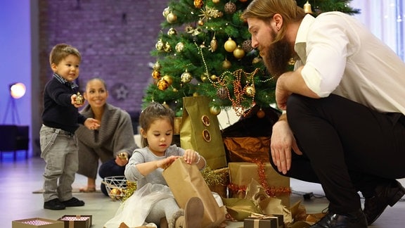 Kinder und Erwachsene packen zusammen Geschenke aus.