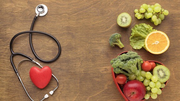 Obst, Gemüse und ein Stetoskop auf einem Holztisch.