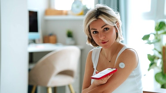 Eine junge Frau misst mit einem Smartphone den Blutzuckerspiegel