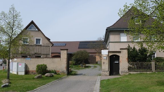 Hofeinfacht und Hof, bebaut mit zwei schon älteren, verputzten Häusern. Hintergrund: Neues Gebäude wie Scheune mit Solarpanelen.