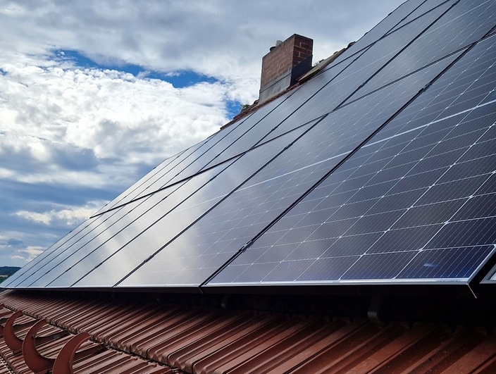 Typische Panele einer Photovoltaik-Anlage auf einem Dach eines Hauses mit roten neueren Ziegeln