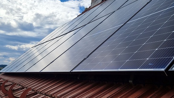 Typische Panele einer Photovoltaik-Anlage auf einem Dach eines Hauses mit roten neueren Ziegeln