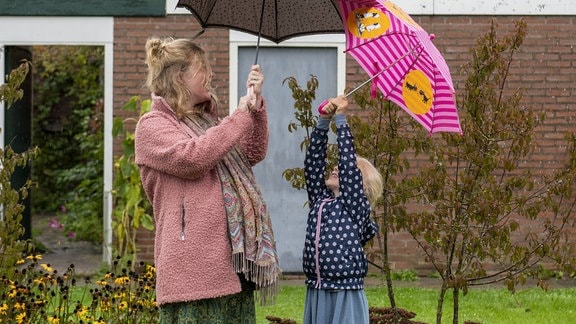 Eine Mutter steht mit ihrer Tochter unter Regenschirmen im Regen.