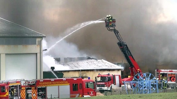 Feuerwehrleute löschen Brand und stehen auf Drehleiter in Rauch zwischen brennenden Ställen