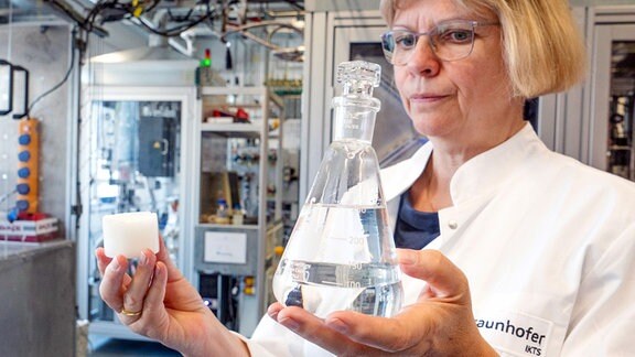 Eine Forscherin zeigt synthetische Kraftstoffe in einem Glaskolben und einen Würfel Biowachse