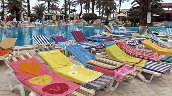 Sonnenliegen, an einem Pool, belegt mit Handtüchern.